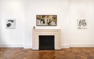 Libbie Mark painting at center. Photo courtesy of Rosenberg & Co., New York; Perle Fine artworks (left and right) courtesy of Berry Campbell, New York. The wall in a gallery with parquet wood flooring featuring a painting over a fireplace.